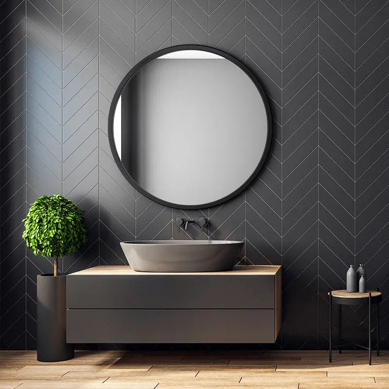 Moderne ronde badkamerspiegel met zwarte rand boven zwevend badkamermeubel met waskom – strak design interieur met donkere wandtegels.