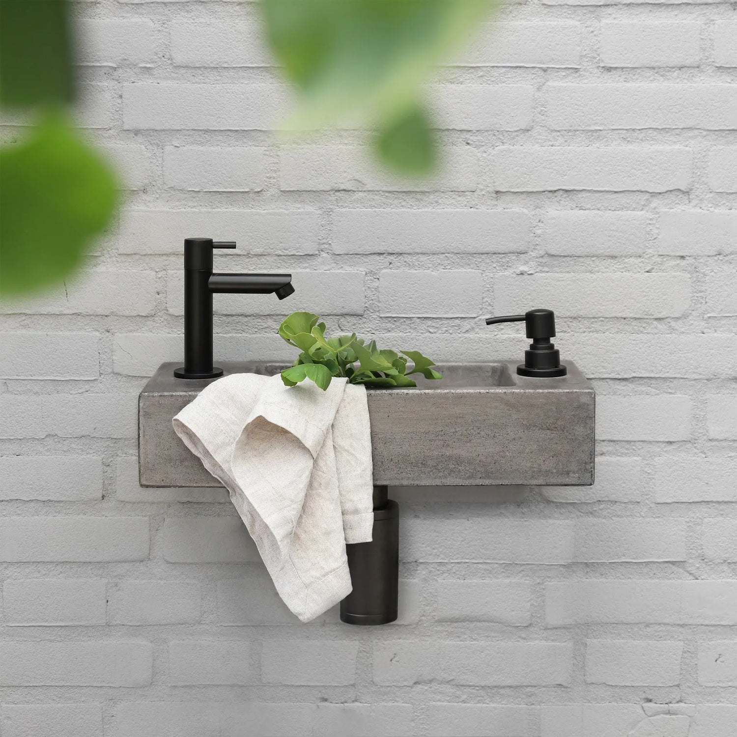 Moderne fontein met betonnen wastafel, mat zwarte toiletkraan en zeepdispenser aan grijze bakstenen muur