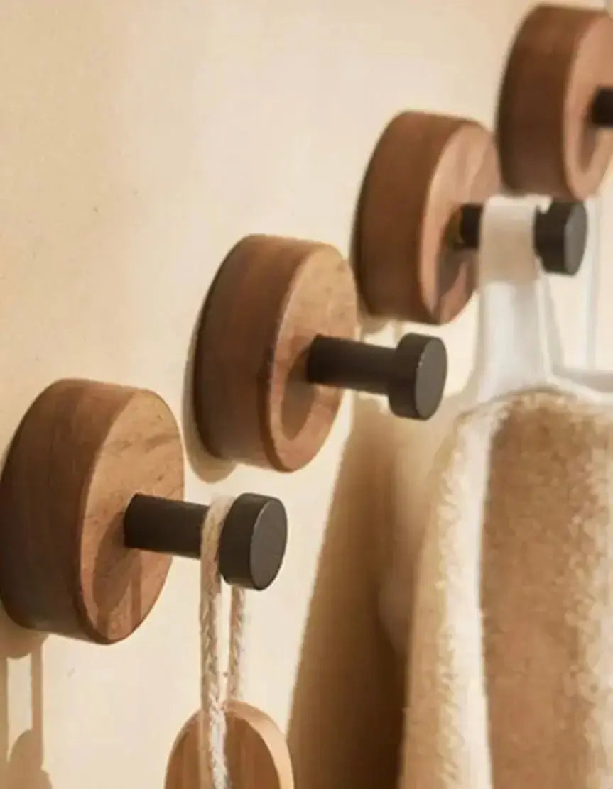 Houten ronde handdoekhaakjes met zwarte haak in een badkamer, gebruikt om handdoeken en accessoires op te hangen.