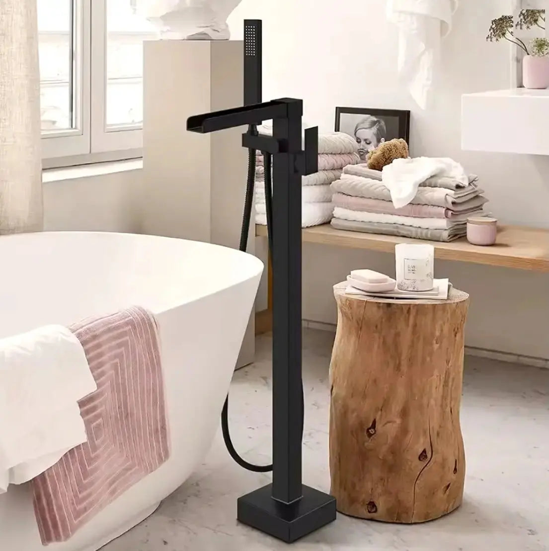 Zwarte vrijstaande badkraan naast een modern wit vrijstaand bad in een warme, stijlvol ingerichte badkamer met natuurlijke materialen.