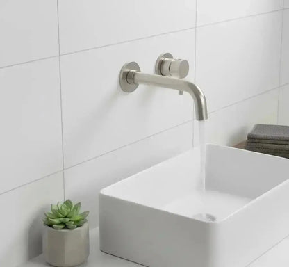 Moderne badkamer met Stria inbouw wastafelmengkraan afbouwdeel in geborsteld RVS, gemonteerd boven een witte rechthoekige opbouw wasbak op een houten plank, met de kraan geopend en water stromend.